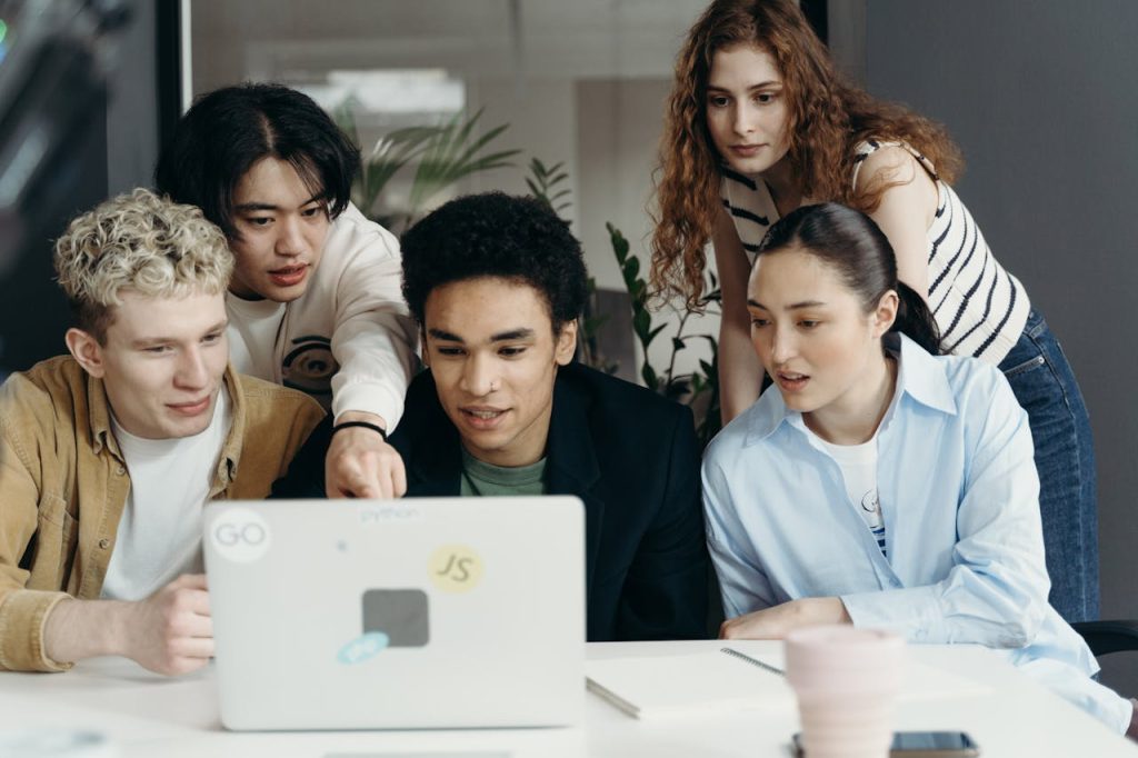 Diverse group of young professionals collaborating on a laptop project in a modern office setting.